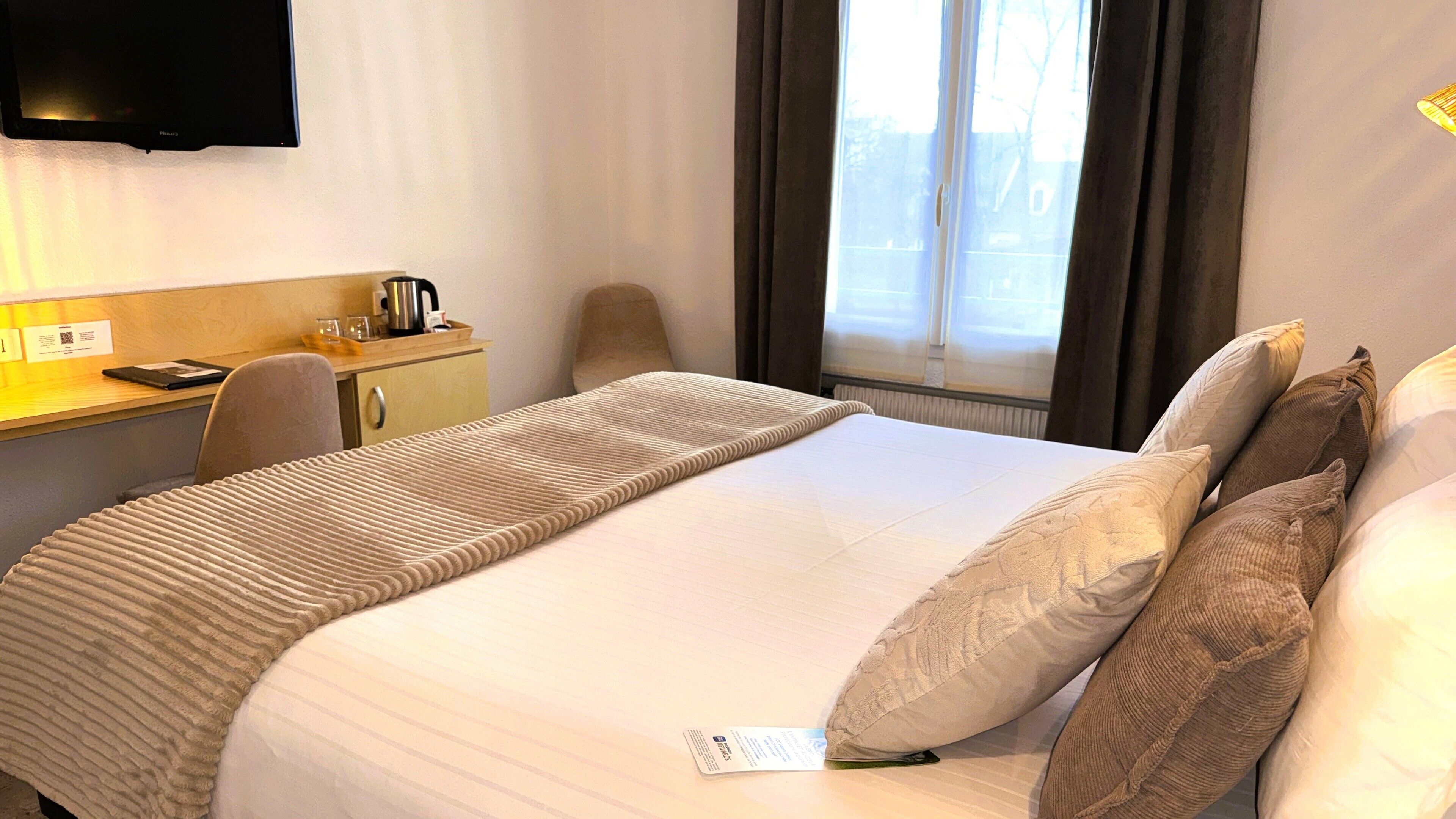 A hotel room with a bed, a desk, a chair, a television, and a window with curtains.