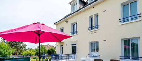 A terrace with wicker furniture, a pink umbrella, and a building with balconies.