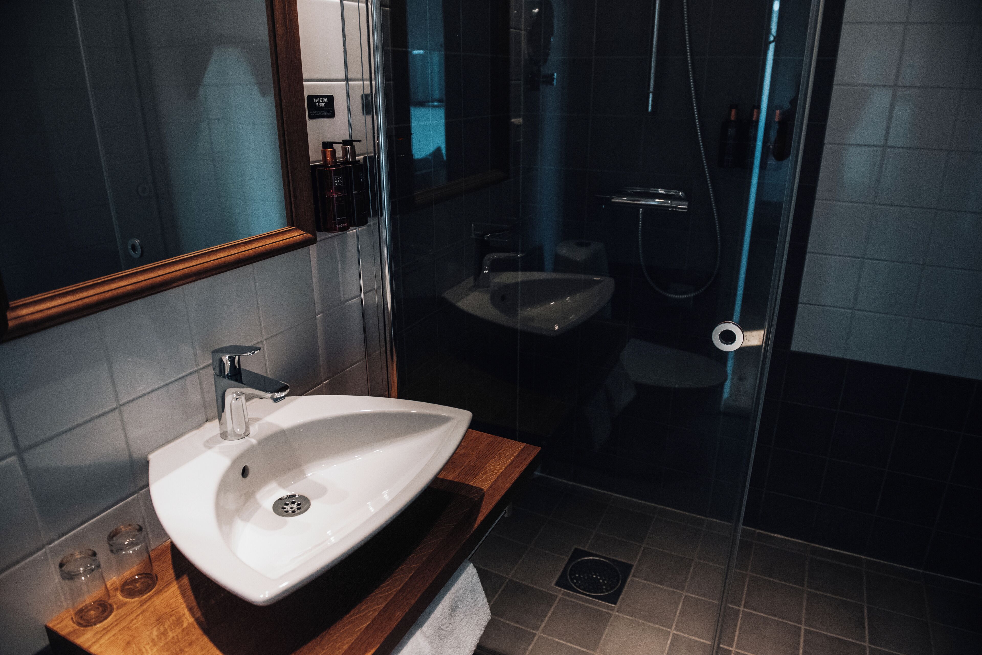 A modern bathroom with a white sink, wooden countertop, and a glass shower enclosure.