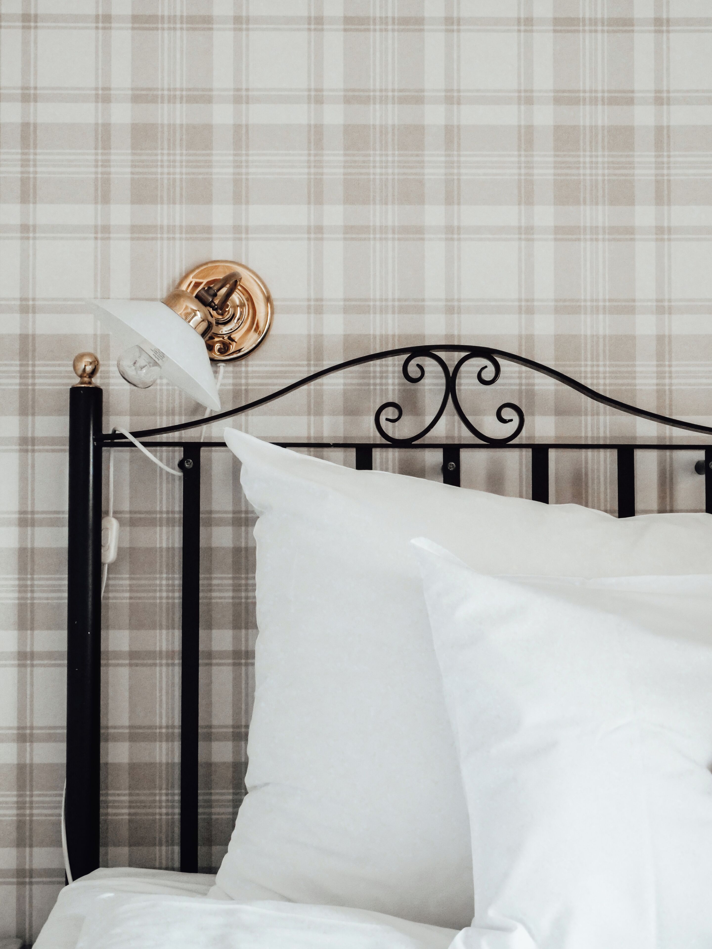 A bed with white bedding and a black metal headboard against a plaid-patterned wall.