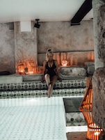 Una persona sentada en un banco estampado en una habitación con suelo de baldosas y pared de piedra.