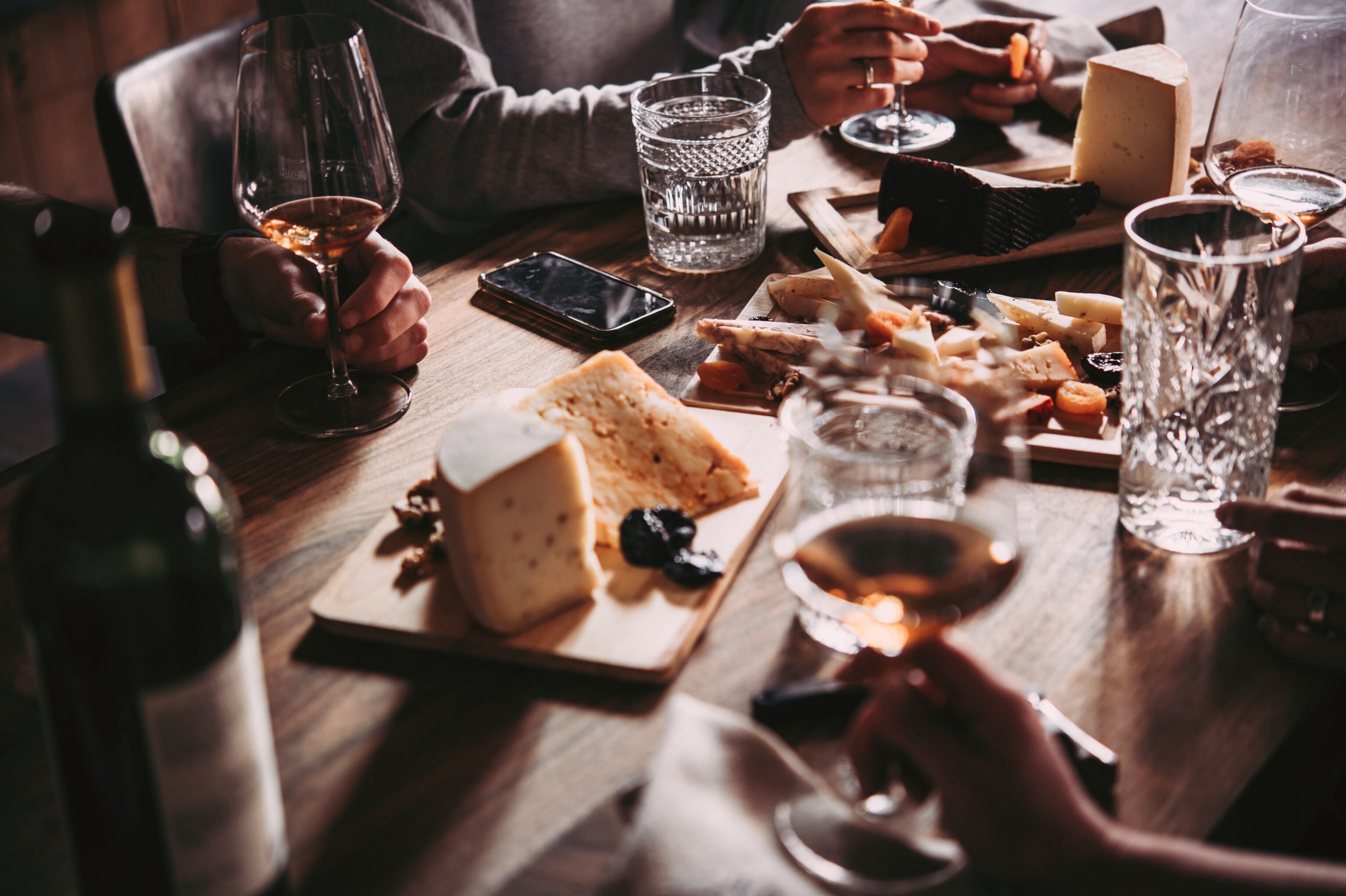 A wooden table with various food items and glasses of wine.