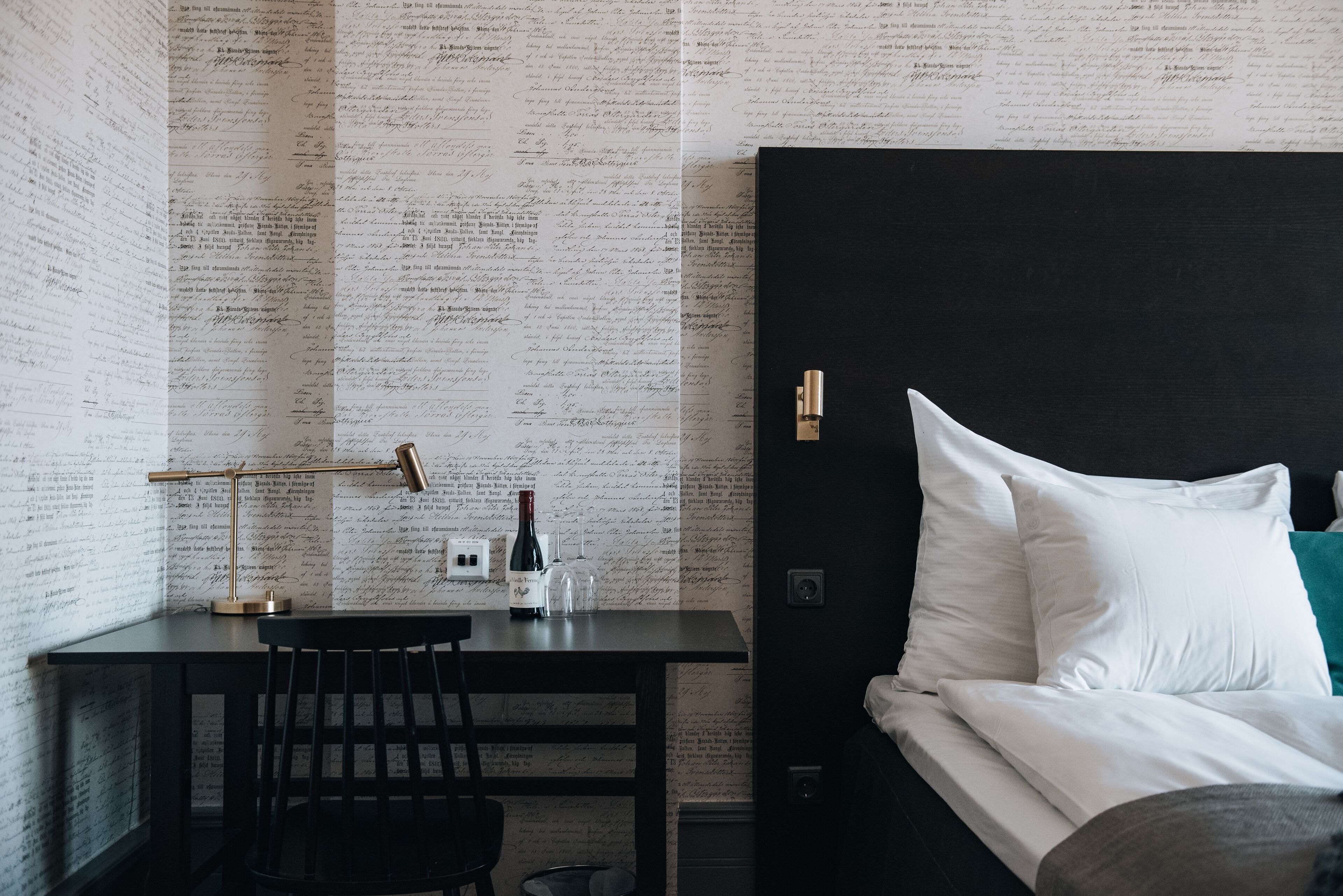 A hotel room with a bed, a desk with a lamp, and a chair.