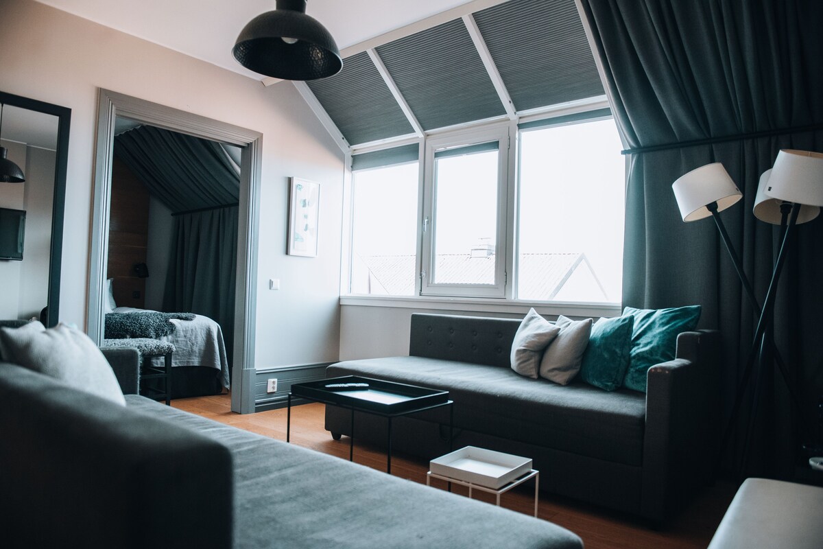 Una sala de estar moderna con un sofá gris, una mesa de centro y un ventanal con cortinas.