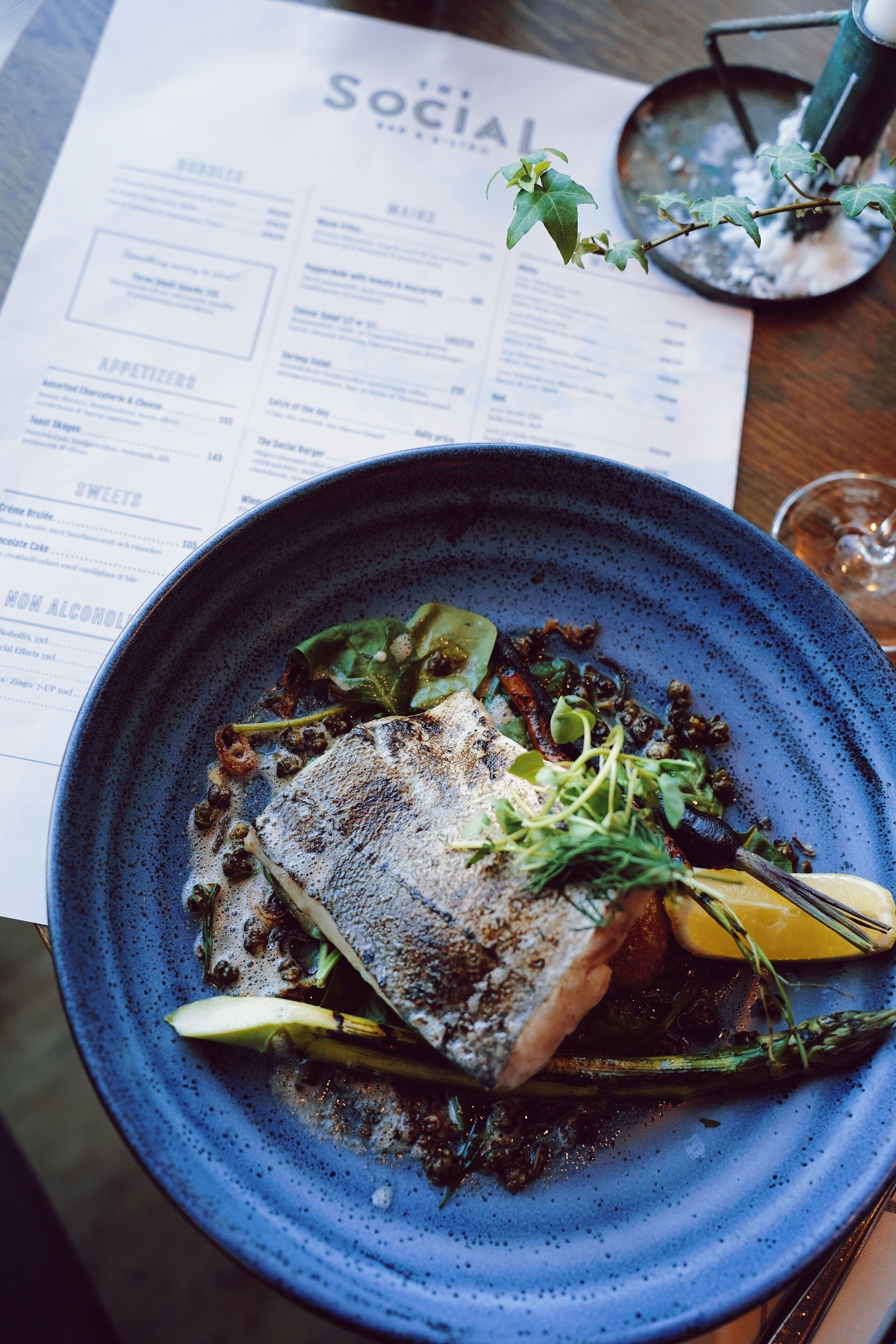 A menu with various food items and a plate of food with a fish, greens, and lemon.