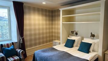 A hotel room with a bed, a chair, a nightstand, and a window with curtains.