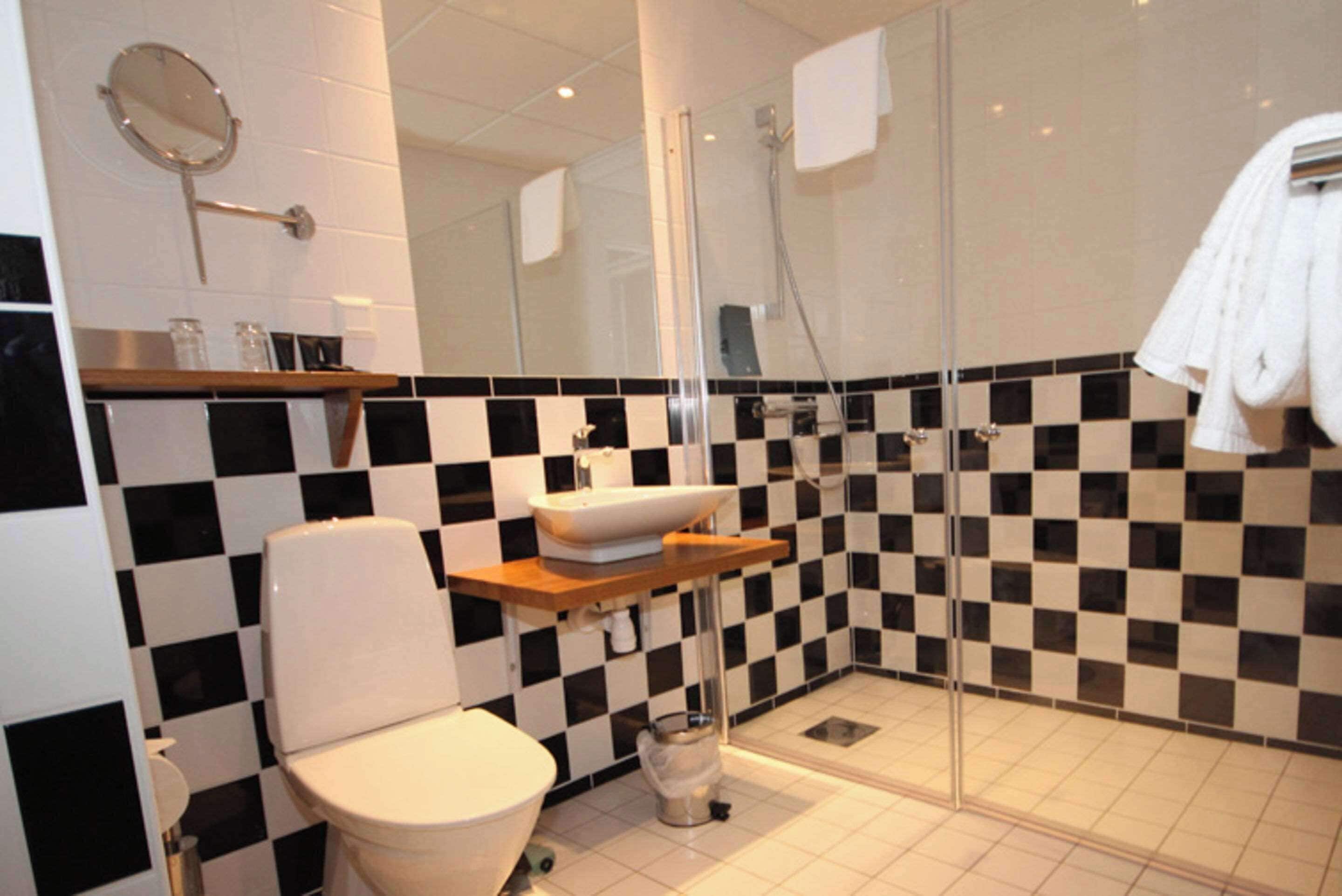 A modern bathroom with a checkered black and white tile backsplash, a white toilet, a glass shower enclosure, and a white towel hanging on the wall.