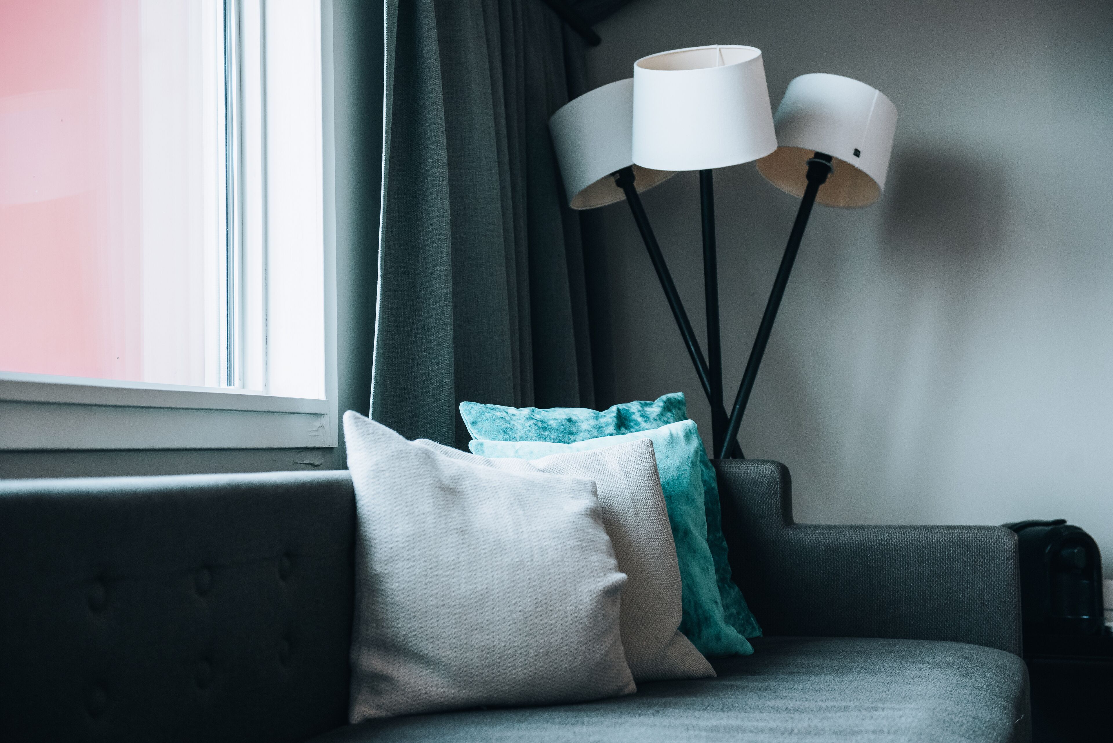 A modern living room with a grey sofa, a floor lamp, and a window with curtains.