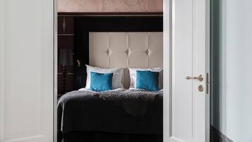 Un dormitorio con cabecera capitonada, dos almohadas, una manta y una puerta con ojo de cerradura.