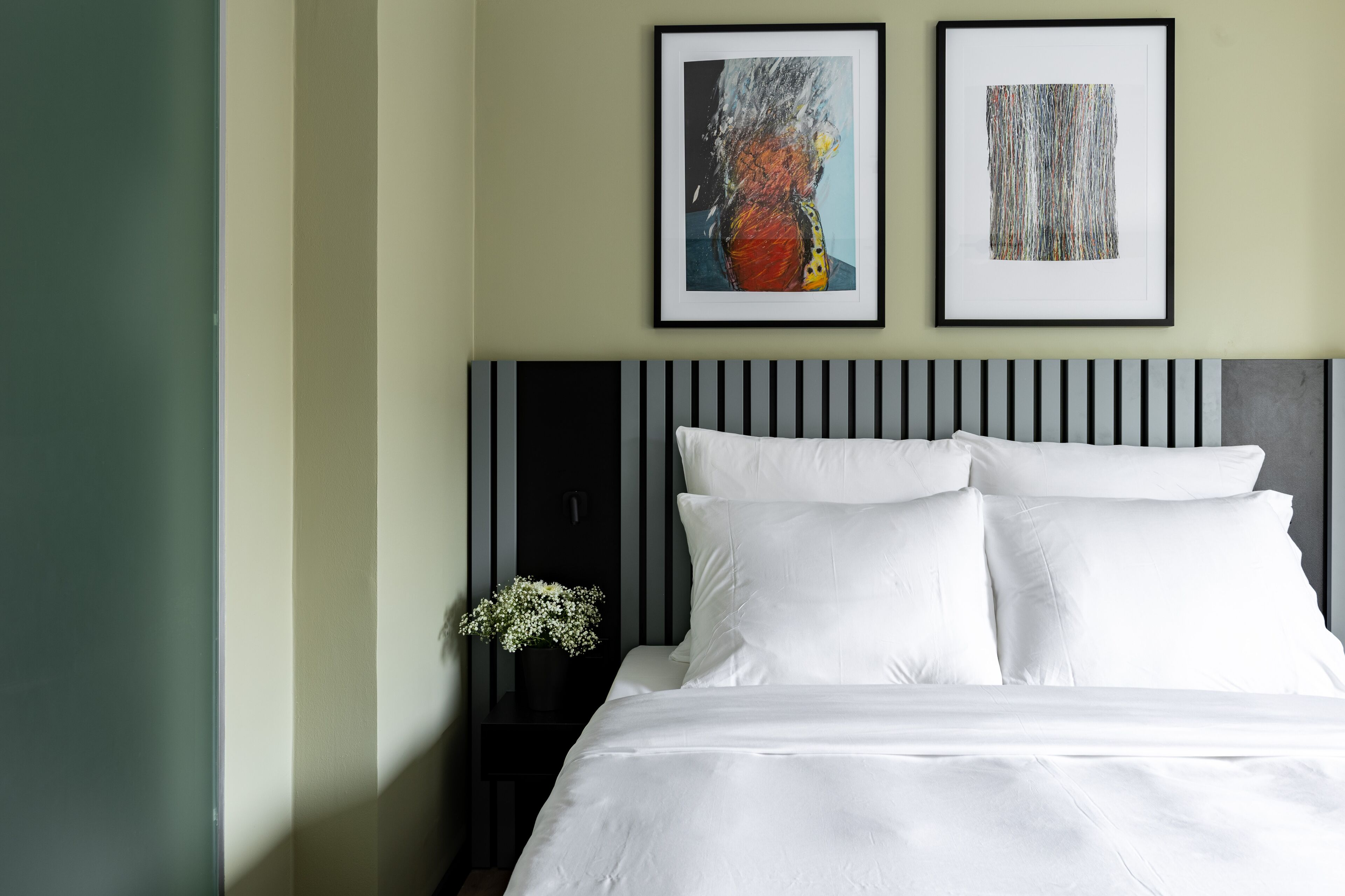 Una cama bien hecha con ropa blanca, un cabecero a rayas negras y blancas y dos cuadros abstractos enmarcados en la pared.