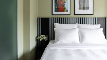 Una cama bien hecha con ropa blanca, un cabecero a rayas negras y blancas y dos cuadros abstractos enmarcados en la pared.