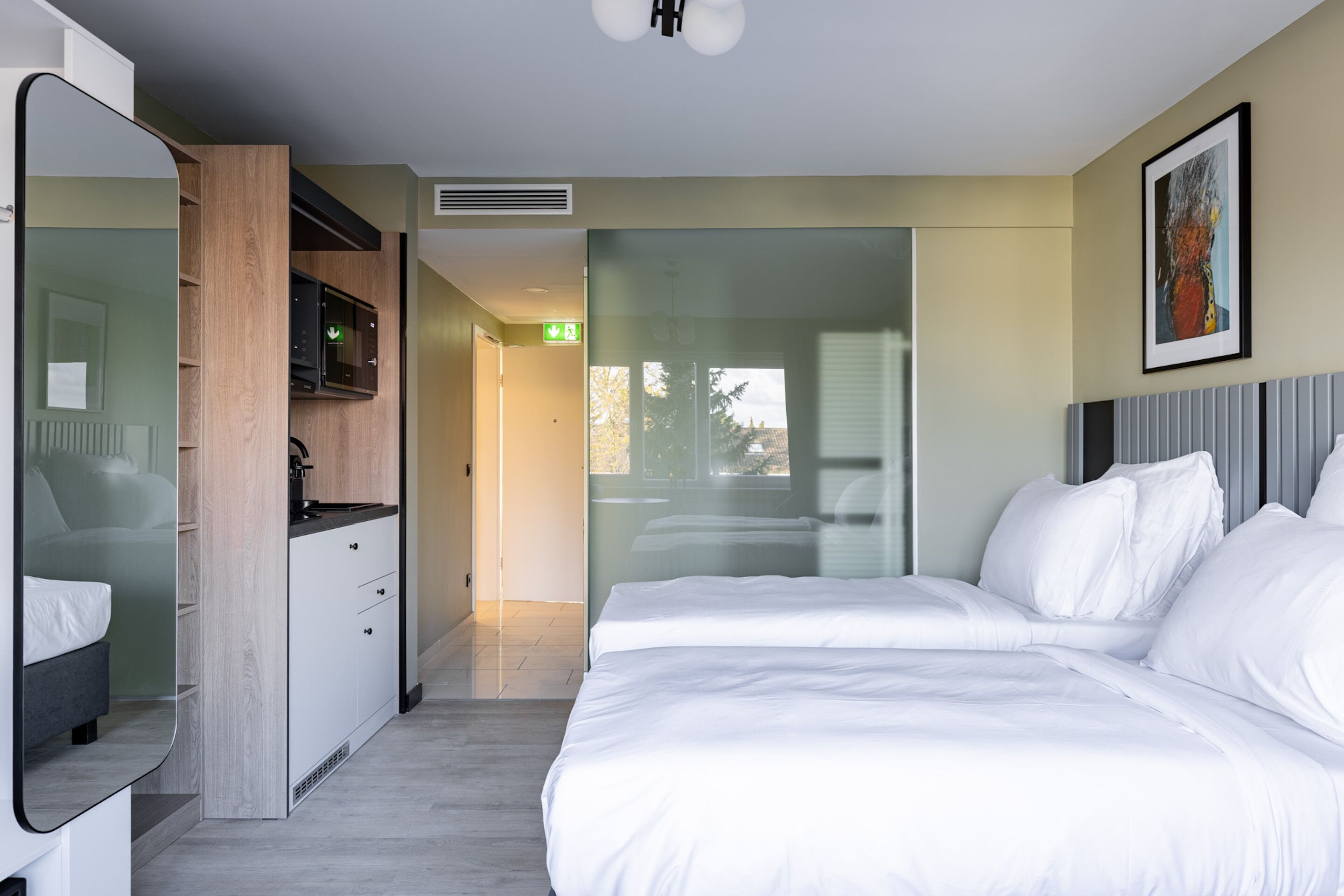 Et moderne hotelværelse med en stor seng, indbygget garderobe, et spejl og udsigt til det fri.