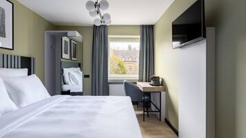 A hotel room with a bed, a desk, a chair, a TV, and a window with curtains.