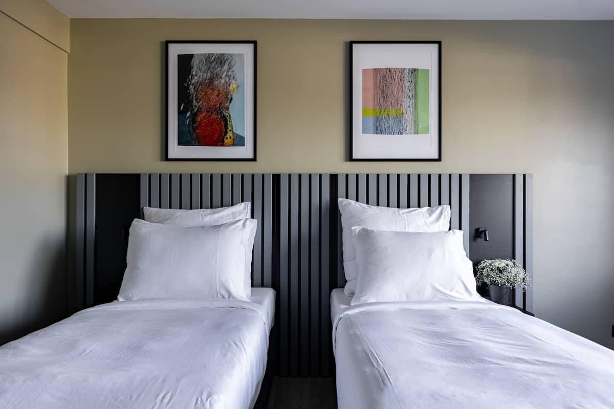 Quarto de hotel com duas camas, um painel de cabeceira listrado e duas obras de arte emolduradas na parede.