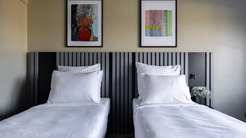 Ein Hotelzimmer mit zwei Betten, einem gestreiften Kopfteil und zwei gerahmten Kunstwerken an der Wand.