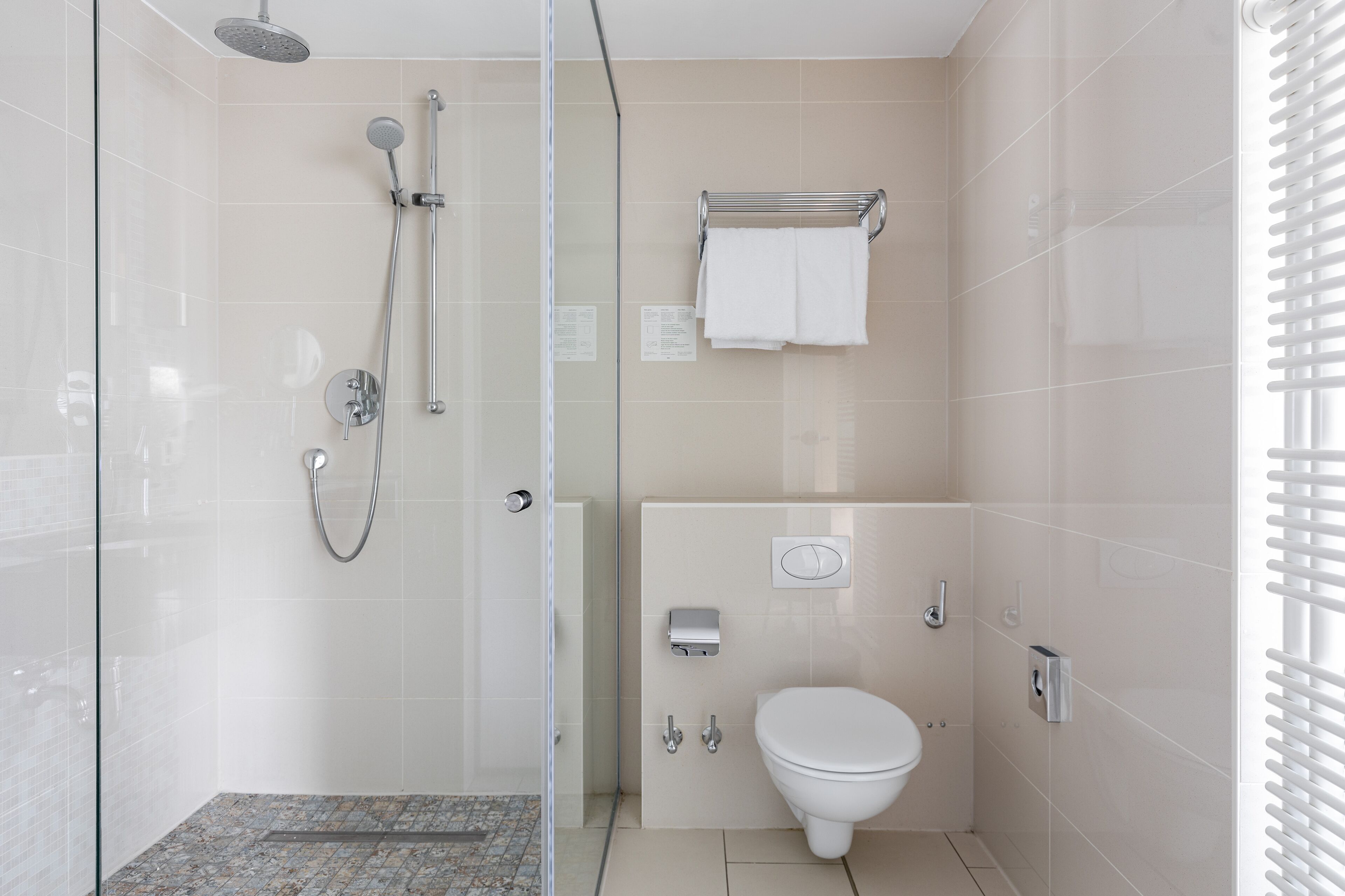 Uma casa de banho moderna com cabine de duche em vidro, sanita branca e barra de toalhas.