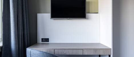 Une chambre moderne avec un téléviseur à écran plat fixé au mur, un bureau de couleur claire et une chaise bleue.