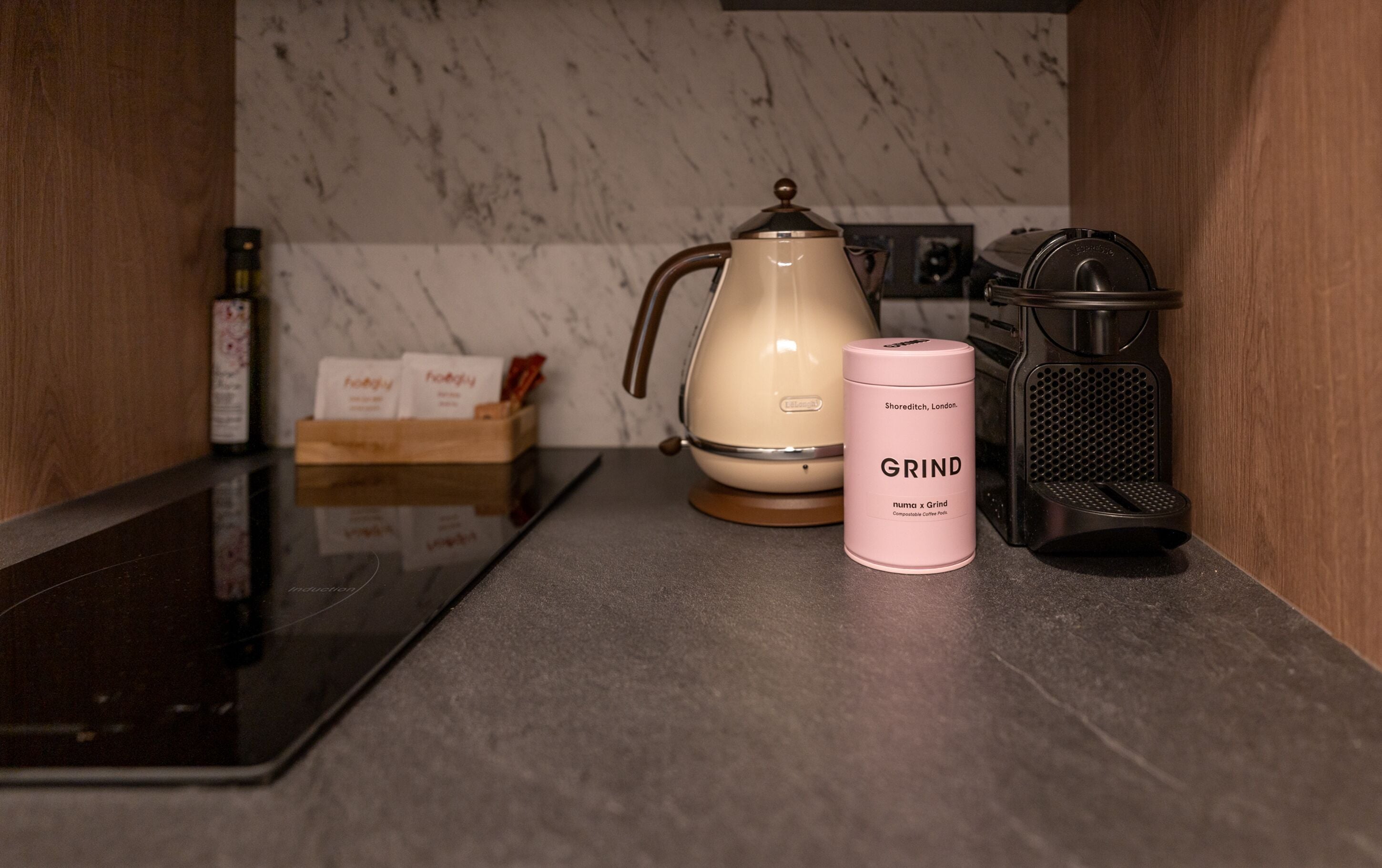 Una encimera de cocina con una cafetera, un molinillo y una caja de cápsulas de café.