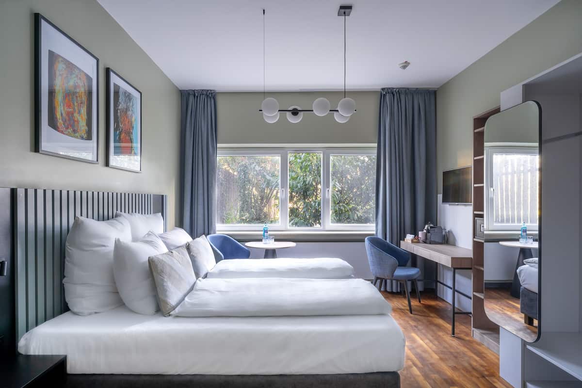 Quarto de hotel moderno com uma cama grande, uma escrivaninha, uma cadeira e uma janela com cortinas.