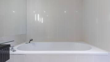 Une salle de bain moderne avec une grande baignoire, un miroir et un plan de toilette noir.