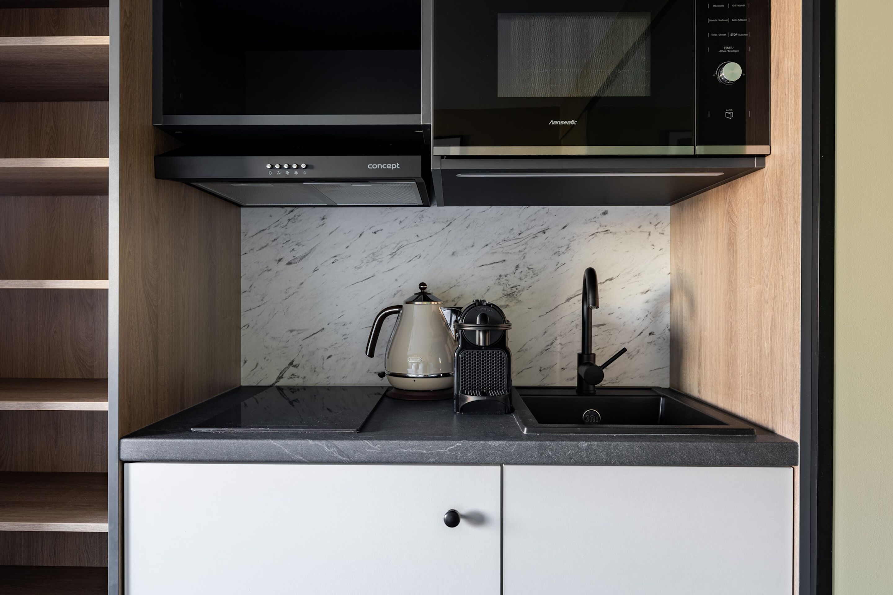 Une cuisine compacte dotée d’un four à micro-ondes, d’une bouilloire et d’une machine à café intégrés, le tout installé sur un plan de travail en marbre.