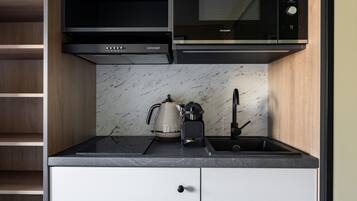 Een kleine keuken met een ingebouwde magnetron, waterkoker en koffiezetapparaat op een marmeren aanrecht.