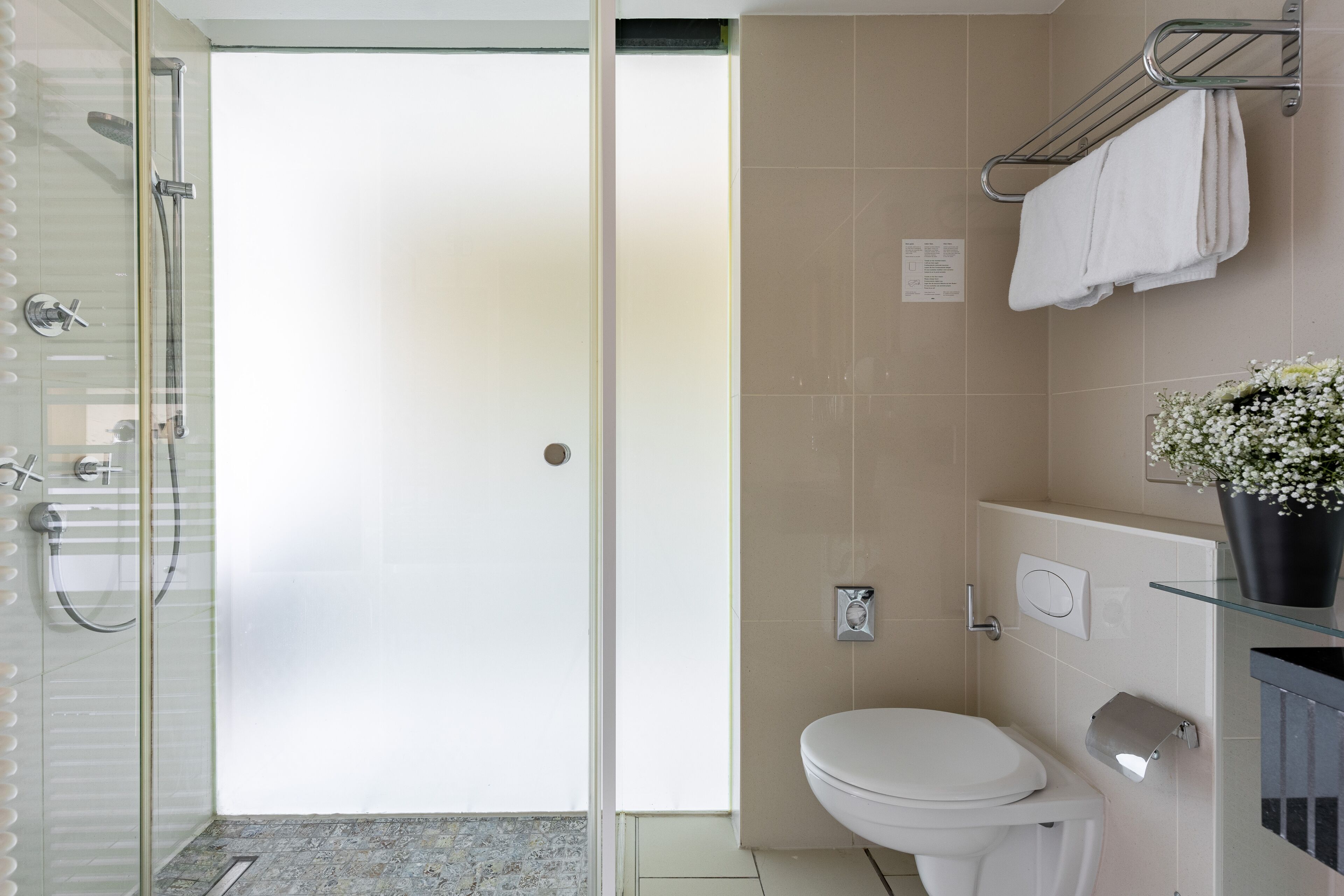 A modern bathroom with a glass shower enclosure, a white toilet, and a glass shelf with a potted plant.
