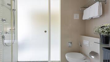 A modern bathroom with a glass shower enclosure, a white toilet, and a glass shelf with a potted plant.