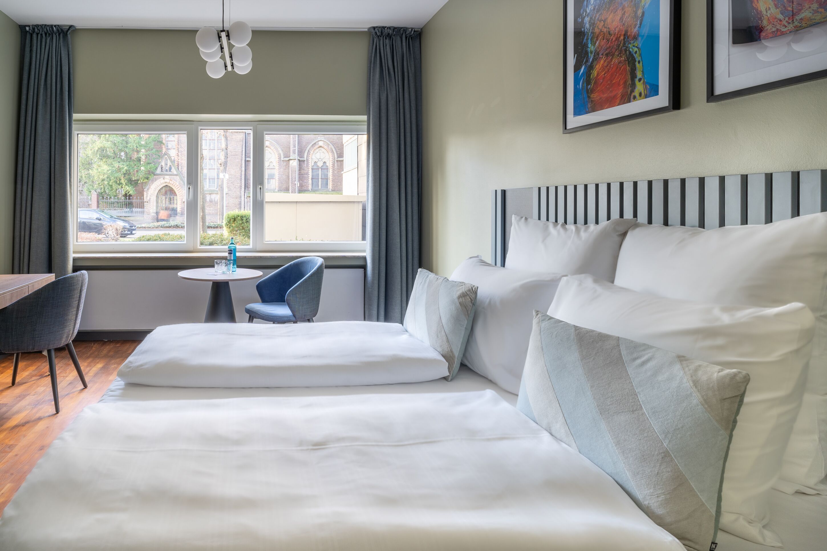 Une chambre d’hôtel avec un grand lit, une petite table ronde, une chaise et une vue sur un immeuble par la fenêtre.