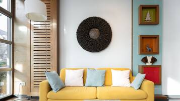 Una sala de estar moderna con un sofá amarillo, un adorno redondo en la pared y fotografías enmarcadas.
