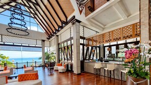 A spacious indoor area with a wooden floor, seating arrangements, a bar area, and large windows offering a view of the ocean. - Garden Cliff Resort and Spa (Pattaya)