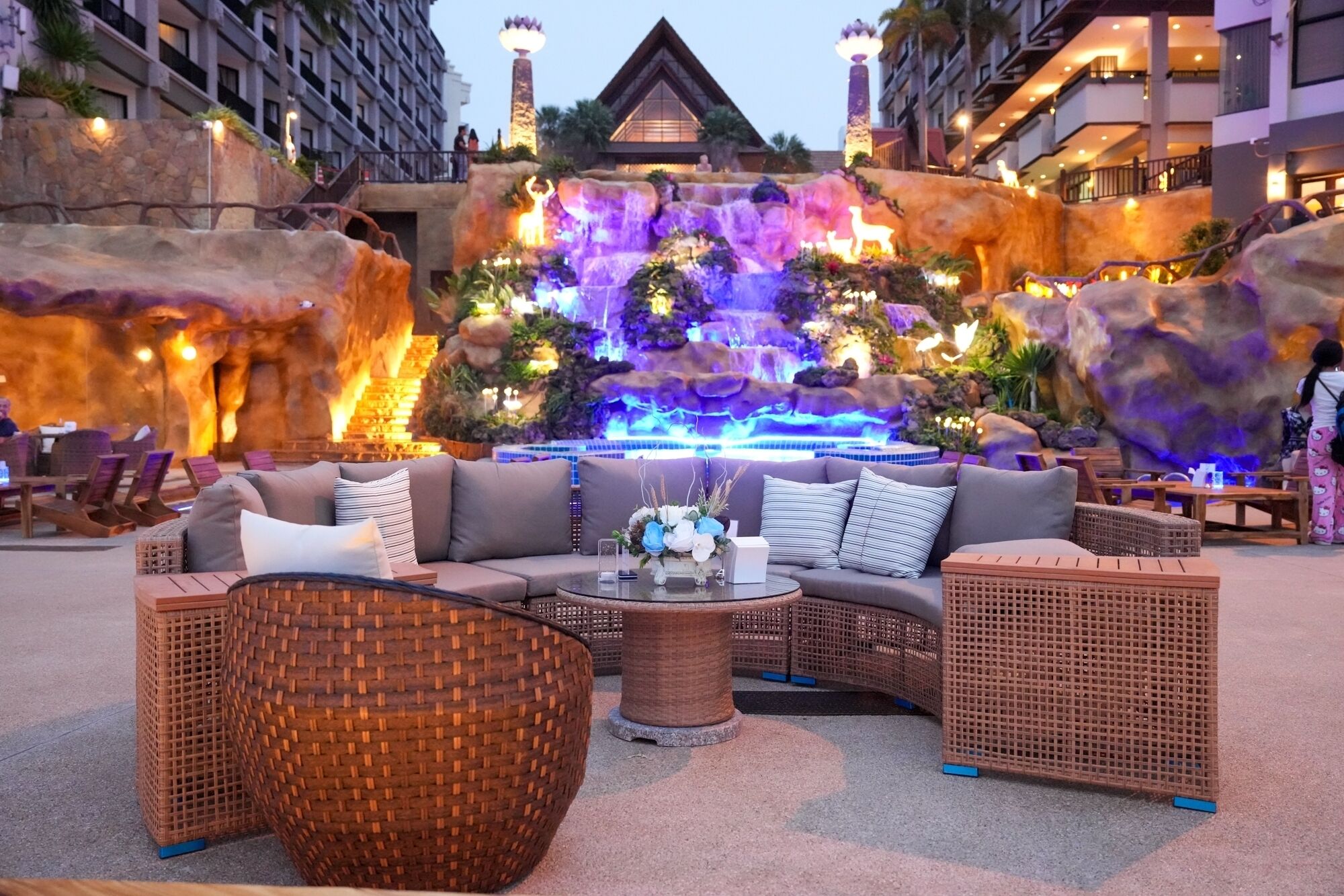 Un espace détente comprenant un canapé, des fauteuils en osier, une table basse et une fontaine décorative.