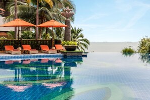 Relax by the serene pool surrounded by lush greenery and palm trees, with lounge chairs and umbrellas for a tranquil retreat.