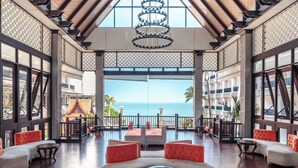A spacious lounge with a view of the ocean, featuring a modern chandelier, red and white seating, and a traditional architectural design. - Garden Cliff Resort and Spa (Pattaya)