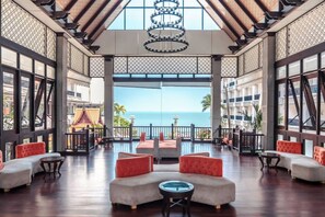 A spacious lounge with a view of the ocean, featuring a modern chandelier, red and white seating, and a traditional architectural design. - Garden Cliff Resort and Spa (Pattaya)
