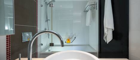 Un baño moderno con lavamanos blanco, grifo cromado y ducha con cerramiento de vidrio.