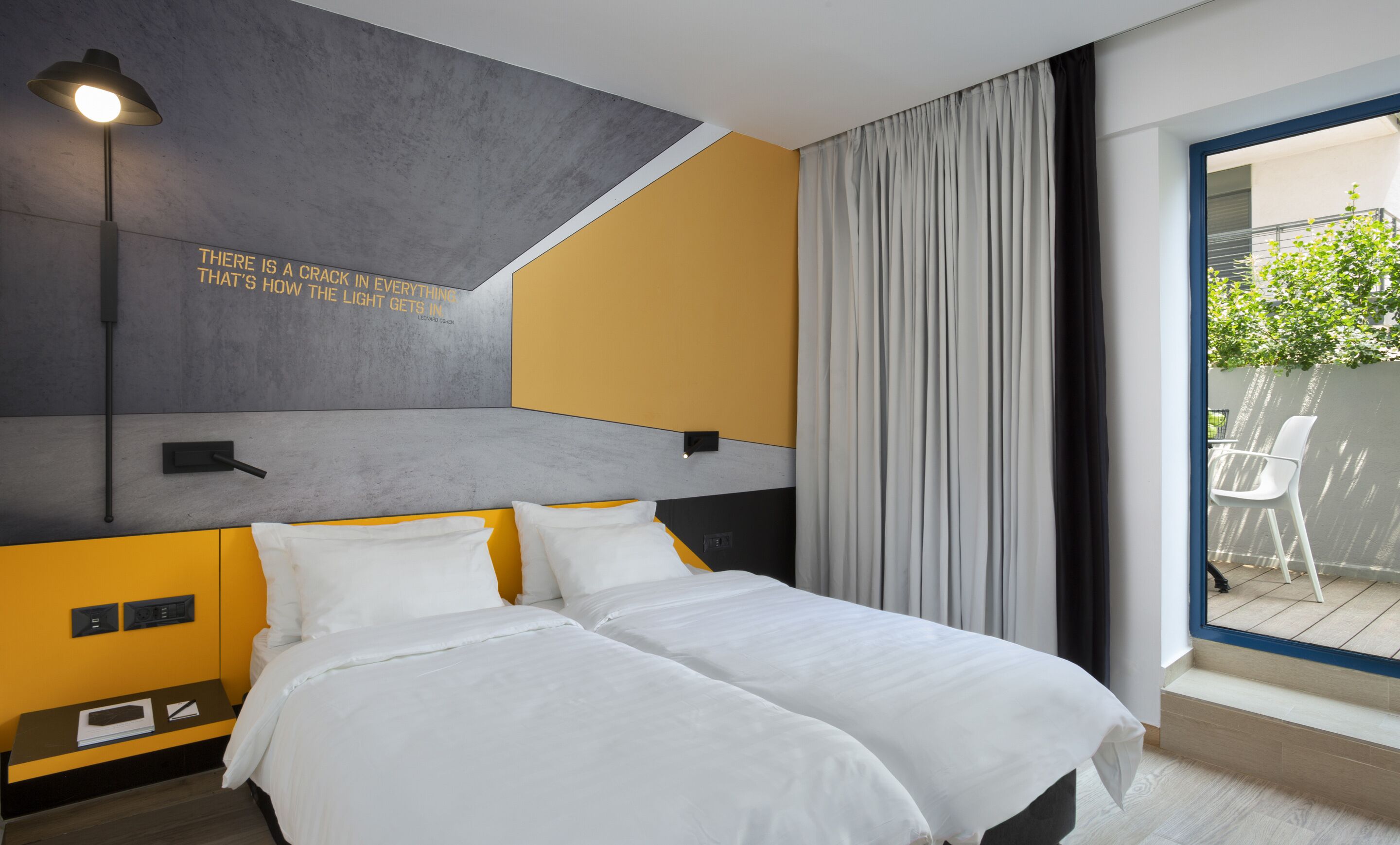 Une chambre d’hôtel moderne, équipée d’un lit, d’une table de chevet, d’une lampe et offrant une vue sur l’extérieur.