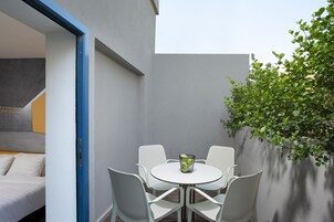A modern outdoor seating area with a round table and white chairs, a small plant, and a wall with a blue trim.