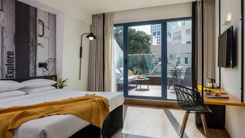 Una habitación de hotel moderna con una cama grande, un escritorio con una silla, televisión y un balcón con vistas a la ciudad.
