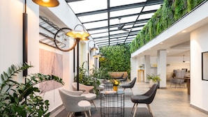 Un espacio interior moderno con techo de vidrio, pared verde y zona de estar con mesas y sillas.