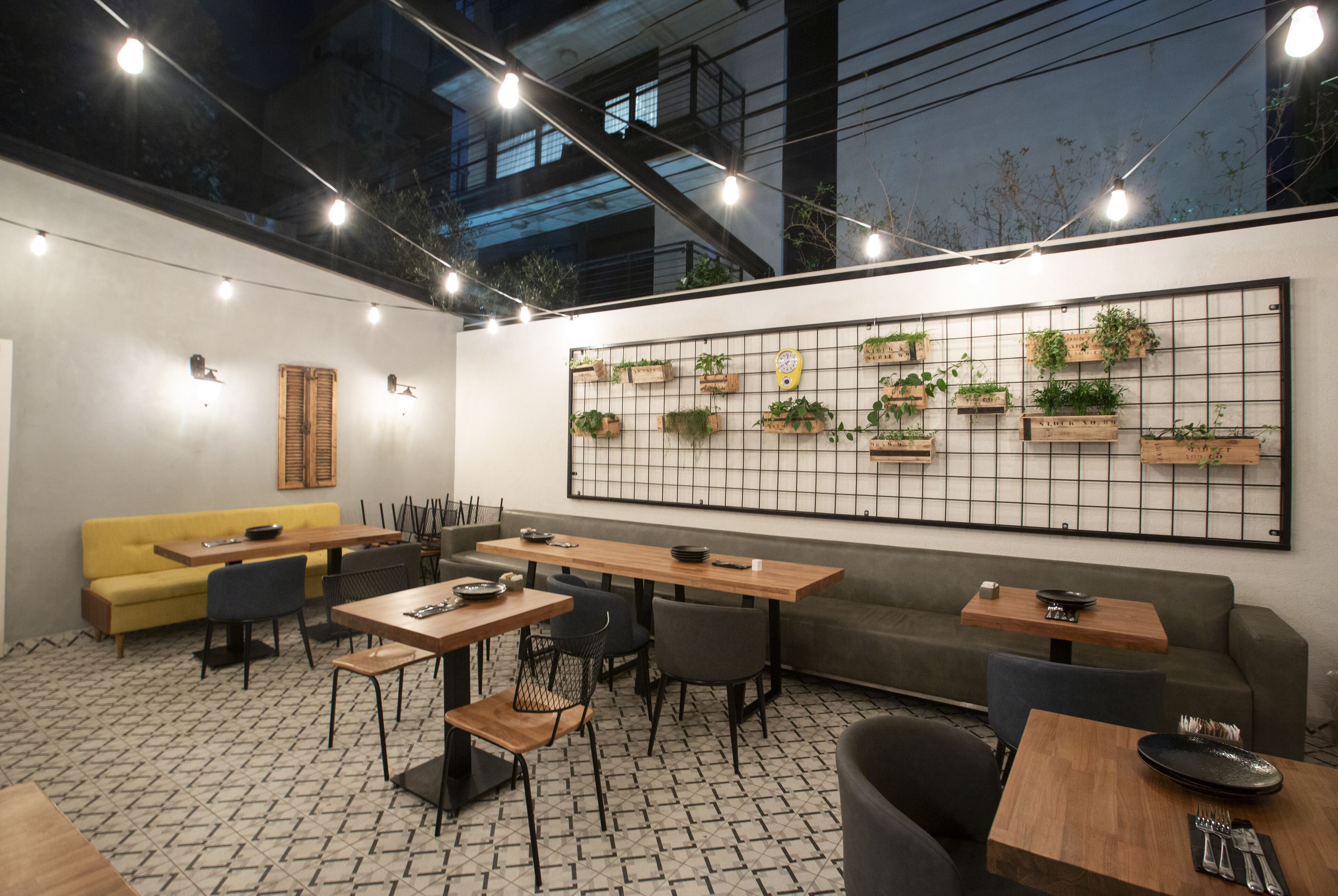 An indoor dining area with tables and chairs, a yellow sofa, and a wall-mounted planter shelf.