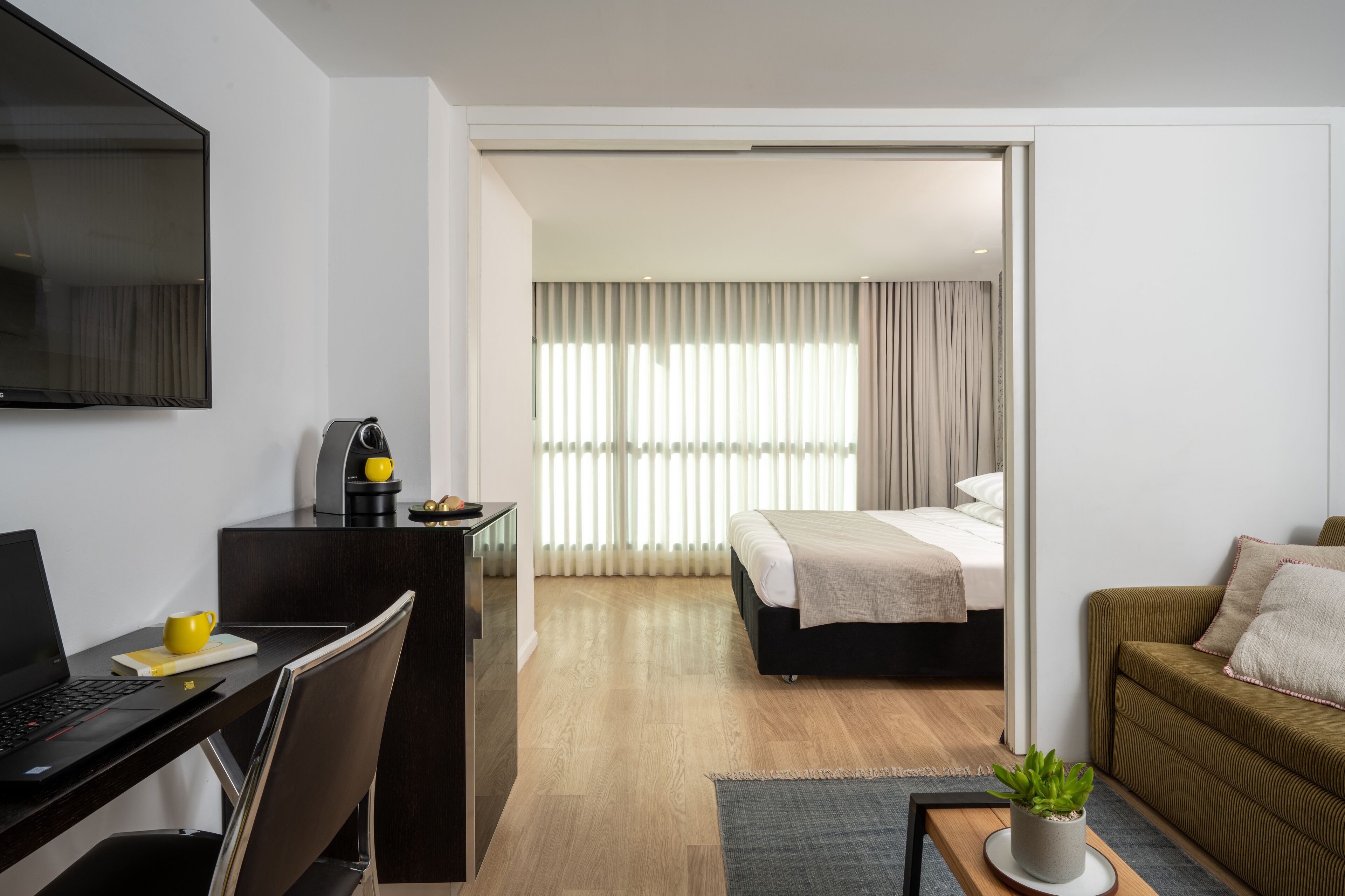 Una habitación de hotel moderna con escritorio, ordenador portátil, cafetera y cama con vista a la ciudad.