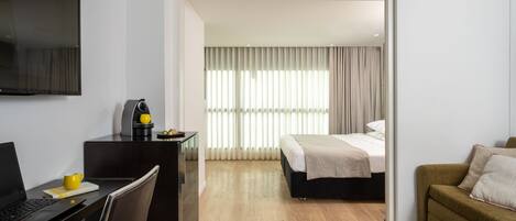 Una habitación de hotel moderna con escritorio, ordenador portátil, cafetera y cama con vista a la ciudad.