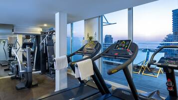 Un gimnasio moderno con cintas de correr y equipo de ejercicio, amplias ventanas con vista a la ciudad.
