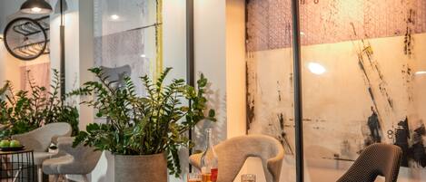 A modern interior with a round table, two chairs, a potted plant, and a wall with abstract art.