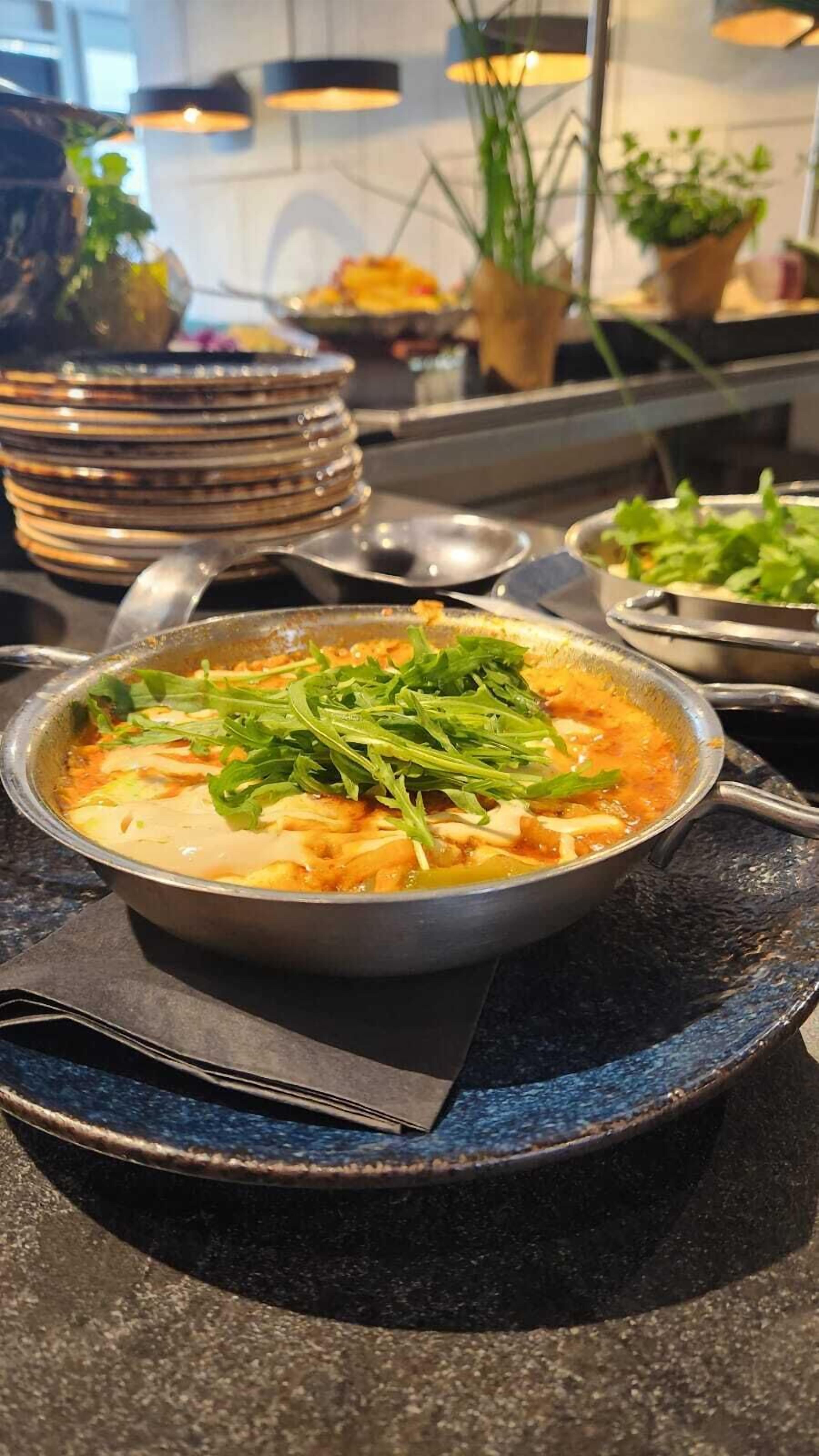 Un tazón de sopa adornado con vegetales, sobre un plato oscuro y con una servilleta debajo.