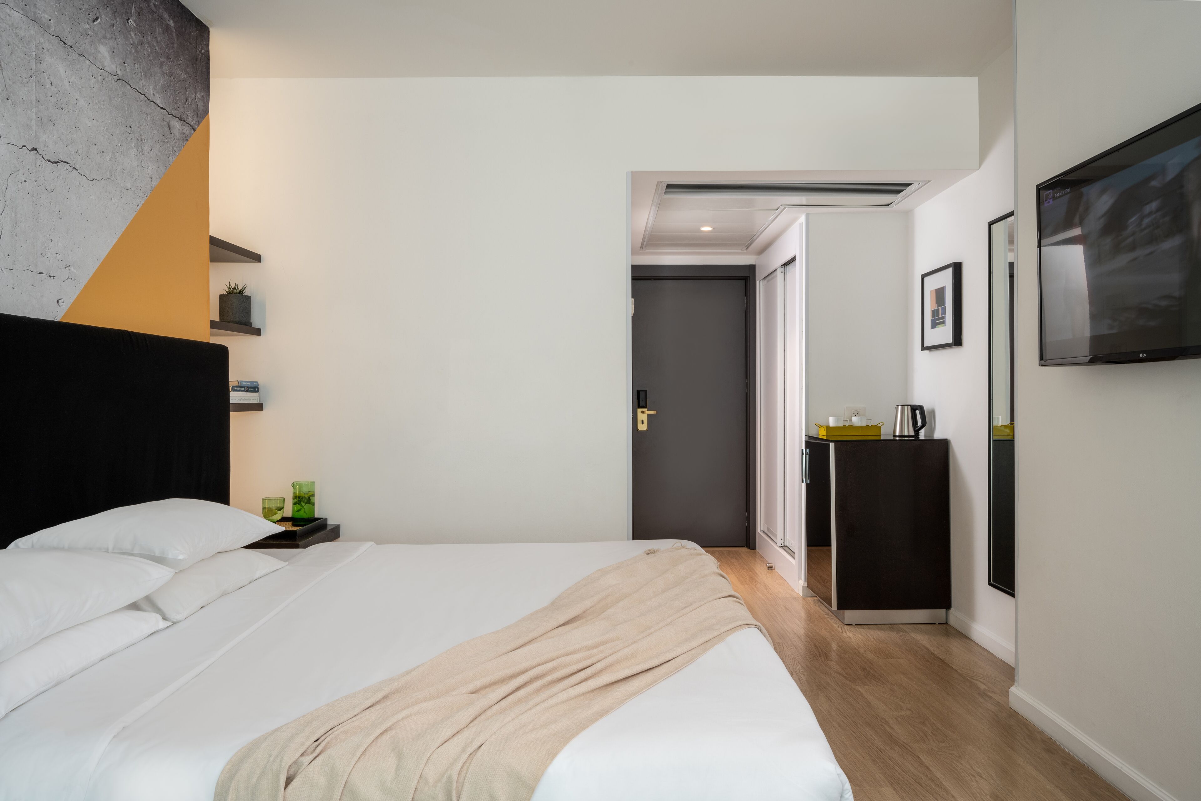 Un hotel moderno con una cama grande, una mesita de noche con lámpara, un armario pequeño y un televisor de pantalla plana montado en la pared.