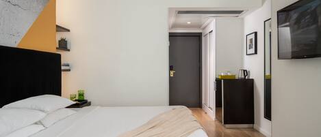 Un hotel moderno con una cama grande, una mesita de noche con lámpara, un armario pequeño y un televisor de pantalla plana montado en la pared.