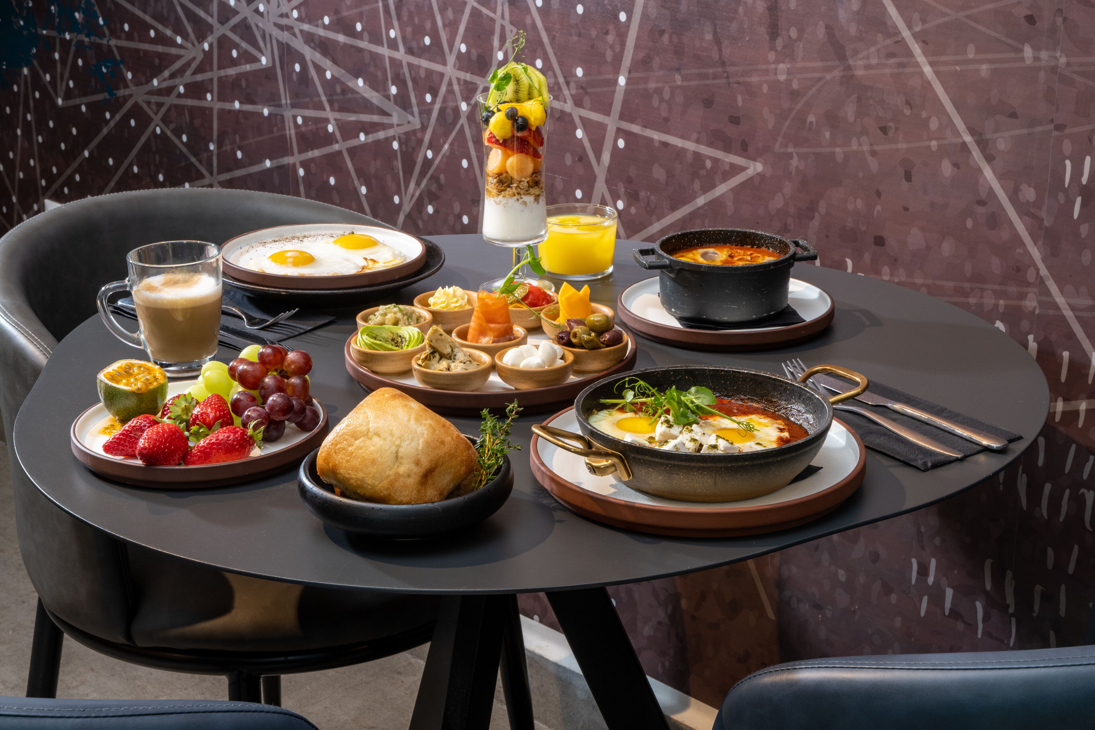 A dining table with breakfast items including eggs, fruit, bread, and a soup dish.