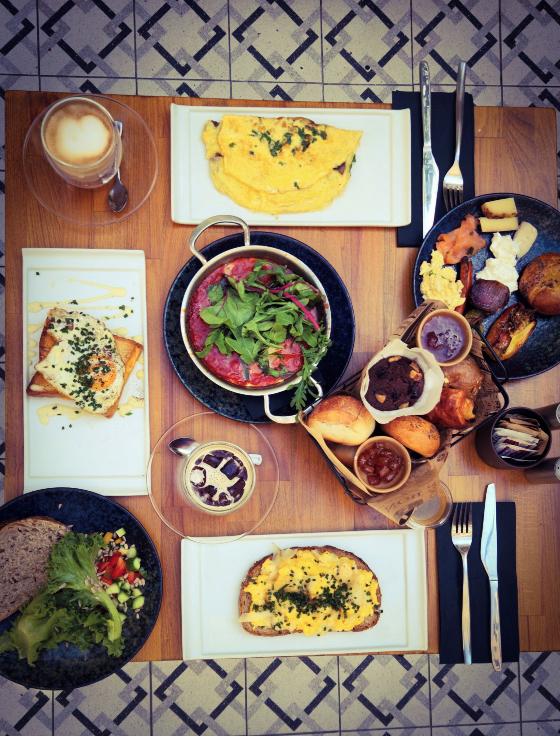 Une table de petit-déjeuner avec divers plats, notamment des toasts, une omelette, une salade et du café.
